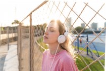 Молода жінка слухає музику на паркані дротяних сіток. — стокове фото