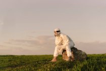 Man wearing protective suit and mask sitting on a rock in the countryside — Stock Photo