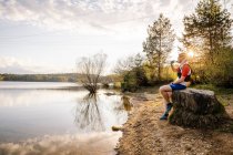 Sportive man sitting on a rock at the lakeside at sunset, Forstsee, Carinthia, Austria — Stock Photo