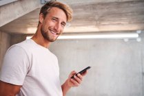 Portrait of attactive young man wearing white t-shirt holding smartphone — Stock Photo