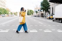 Giovane donna che attraversa la strada usando il cellulare, Barcellona, Spagna — Foto stock