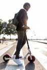 Бізнесмен з рюкзаком і велосипедним шоломом, що перетинає вулицю на штовхаючому скутері на заході сонця — стокове фото