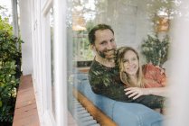 Joyeux couple assis sur le canapé, avec des arns autour, souriant — Photo de stock