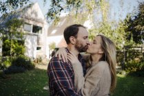 Happy couple kissing in garden, in front of their dream house — Stock Photo