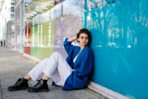 Jeune femme appuyée sur un mur de verre coloré avec sa réflexion — Photo de stock