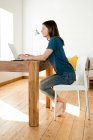Jeune femme travaillant à l'ordinateur portable de la maison dans le bureau à la maison dans le salon moderne — Photo de stock