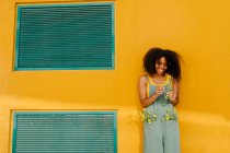 Porträt einer glücklichen jungen Frau in Overalls mit Blumen vor gelber Wand — Stockfoto