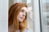 Portrait of serious young woman looking out of window — Stock Photo