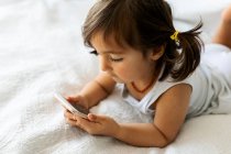Little girl in underwear lying on bed  looking at smartphone — Stock Photo