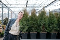 Femme aux yeux fermés s'appuyant sur les plantes vertes dans le magasin de fleurs — Photo de stock