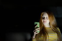 Young woman using smartphone in the dark — Stock Photo