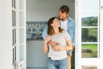Attrayant jeune couple debout dans la porte ensemble à la maison et souriant à l'autre — Photo de stock