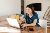 Souriant jeune femme travaillant à l'ordinateur portable de la maison dans le bureau à la maison dans le salon moderne — Photo de stock