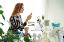 Young woman using smartphone at desk at home — Stock Photo