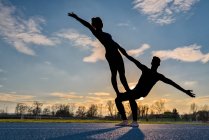 Young couple doing acrobatics at sunset — Stock Photo