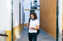 Junger Mann benutzt Handy, während er auf einer engen Straße in Santa Cruz, Sevilla, Spanien, spaziert — Stockfoto
