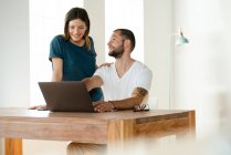 Couple souriant travaillant à l'ordinateur portable de la maison dans le bureau à la maison dans le salon moderne — Photo de stock