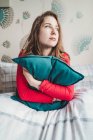 Serious young woman sitting in bed at home hugging cushion — Stock Photo