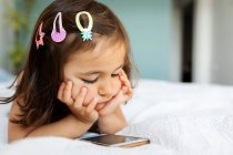 Portrait of little girl lying on bed looking at smartphone — Stock Photo