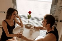 Романтична молода пара з червоною трояндою сидить за кухонним столом. — стокове фото