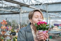 Femme aux yeux fermés reniflant fleurs roses dans la boutique de fleurs — Photo de stock
