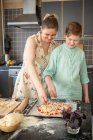 Mother and son scattering grated cheese on pizzy base — Stock Photo