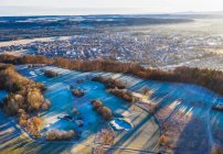 Alemania, Baviera, Wolfratshausen, Drone vista del campo de golf de invierno en frente de la ciudad en las estribaciones alpinas al amanecer - foto de stock