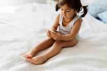 Little girl in underwear sitting on bed  looking at smartphone — Stock Photo