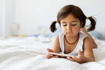 Portrait of little girl lying on bed in underwear looking at smartphone — Stock Photo