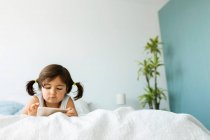 Portrait of little girl lying on bed using at smartphone — Stock Photo