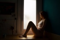 Serious young woman sitting on windowsill at home — Stock Photo