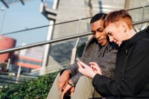 Молодая пара в городе сидит на лестнице, используя мобильный телефон — стоковое фото
