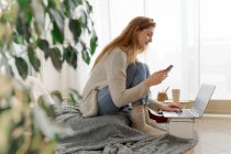 Young woman using smartphone and laptop at home — Stock Photo