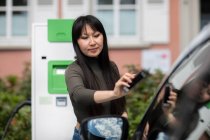 Compartir coche, mujer alquilando un coche eléctrico con smartphone - foto de stock