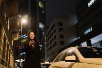 Jovem mulher usando smartphone na cidade à noite, Frankfurt, Alemanha — Fotografia de Stock