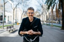 Retrato de un hombre de negocios de pelo gris con bicicleta en la ciudad - foto de stock