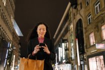 Jovem mulher usando smartphone na cidade à noite, Frankfurt, Alemanha — Fotografia de Stock