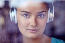 Retrato de mujer joven detrás del cristal de la ventana escuchando música con auriculares - foto de stock