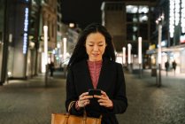 Jovem mulher usando smartphone na cidade à noite, Frankfurt, Alemanha — Fotografia de Stock