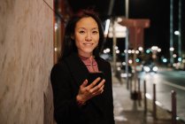 Retrato de uma jovem mulher usando smartphone na cidade à noite, Frankfurt, Alemanha — Fotografia de Stock