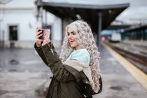 Retrato de una joven riendo tomando selfie con smartphone en la plataforma - foto de stock