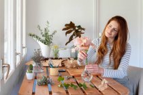 Spain, Portrait of young beautiful redhead woman potting plants at table — Stock Photo