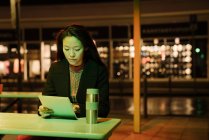 Jeune femme utilisant une tablette sur une terrasse de café dans la ville la nuit, Francfort, Allemagne — Photo de stock