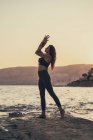 Femme mûre pratiquant le yoga à la plage de rochers le soir — Photo de stock