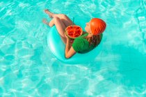 Mujer con neumático flotante y sandía relajante en piscina - foto de stock