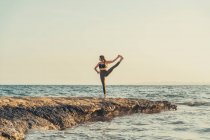 Femme mûre pratiquant le yoga à la plage de rochers le soir — Photo de stock