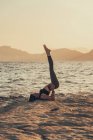 Femme mûre pratiquant le yoga à la plage de rochers le soir — Photo de stock