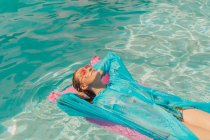 Mujer con abrigo de lluvia azul relajante en cama de aire rosa en la piscina - foto de stock