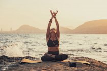Femme mûre pratiquant le yoga à la plage de rochers le soir — Photo de stock