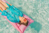 Mujer con abrigo de lluvia azul relajante en cama de aire rosa en la piscina - foto de stock